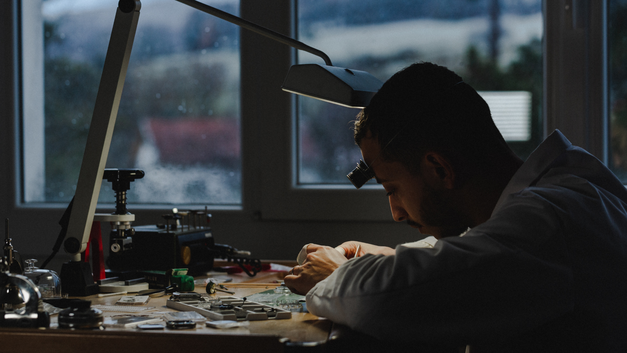 Un horloger qui travaille en blouse dans son atelier sur des montres mécaniques et automatiques