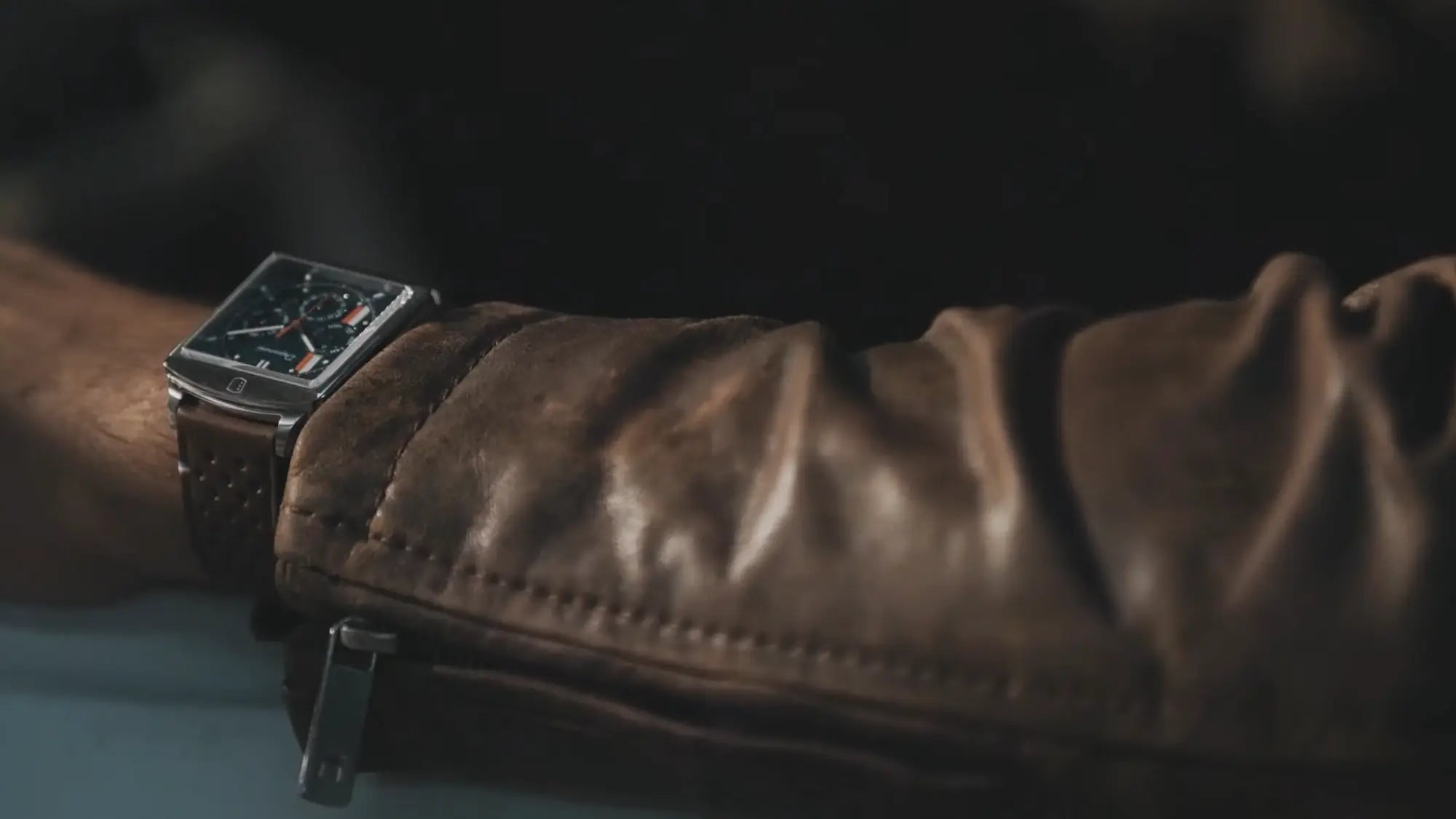 montre depancel française carrée automatique portée au poignet d'un homme portant une veste en cuir marron au volant d'une voiture mustang sportive